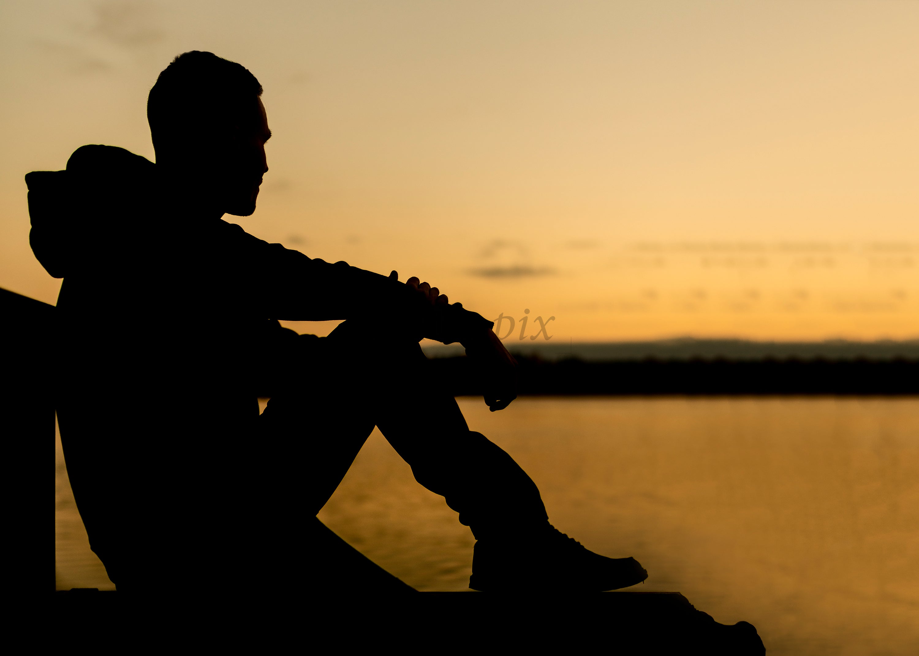 Silhouette of man sitting on dock at sunset