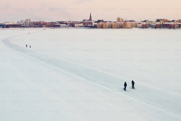 Snowy lake foreground with city center skyline of Luleå during winter calm soft sunset view