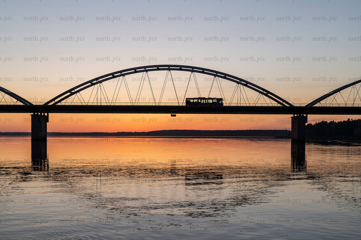 Tram crossing arch bridge over river at sunset